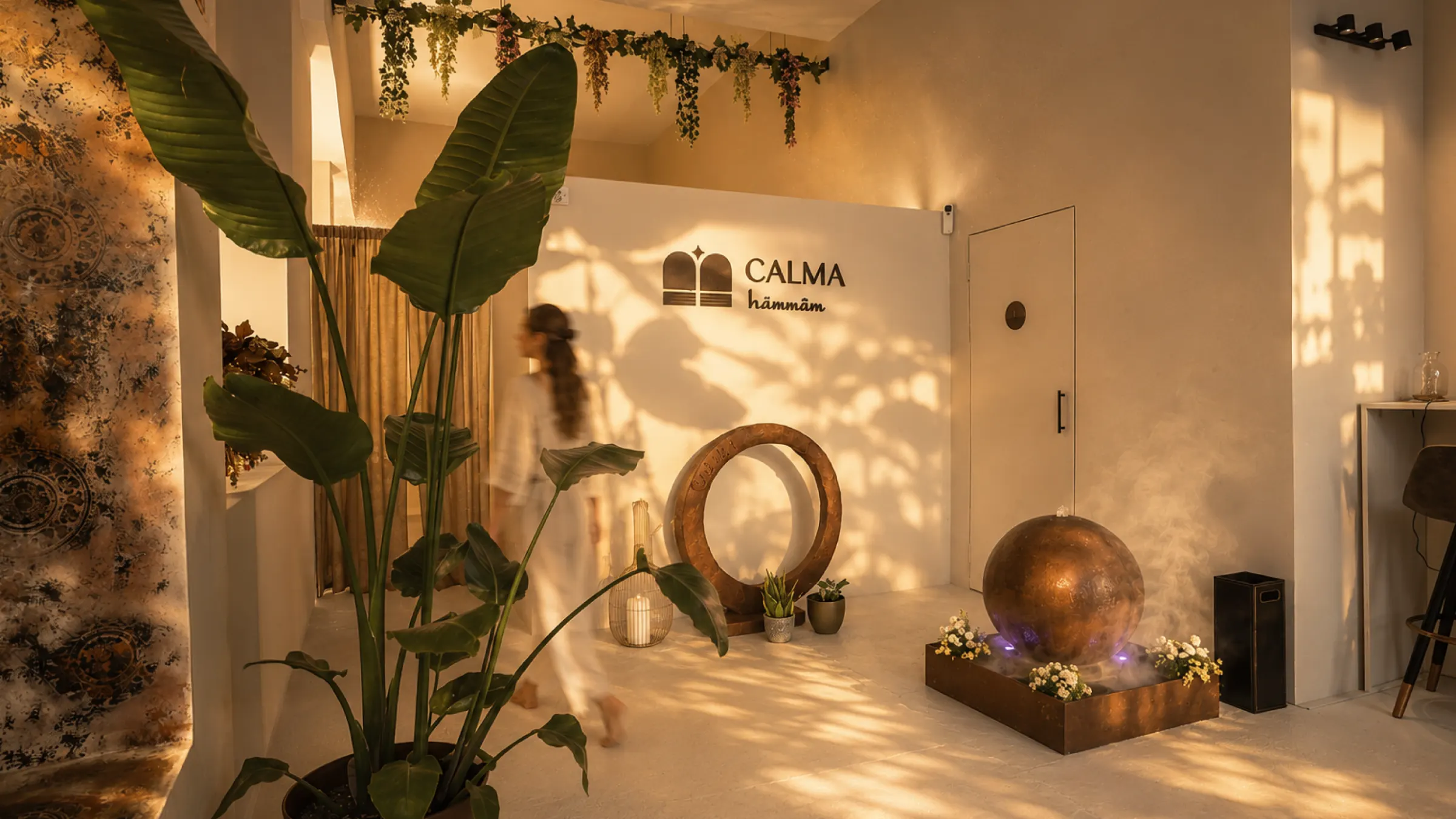 Recepción de Calma Hammam con plantas, luz cálida y el logotipo en la pared