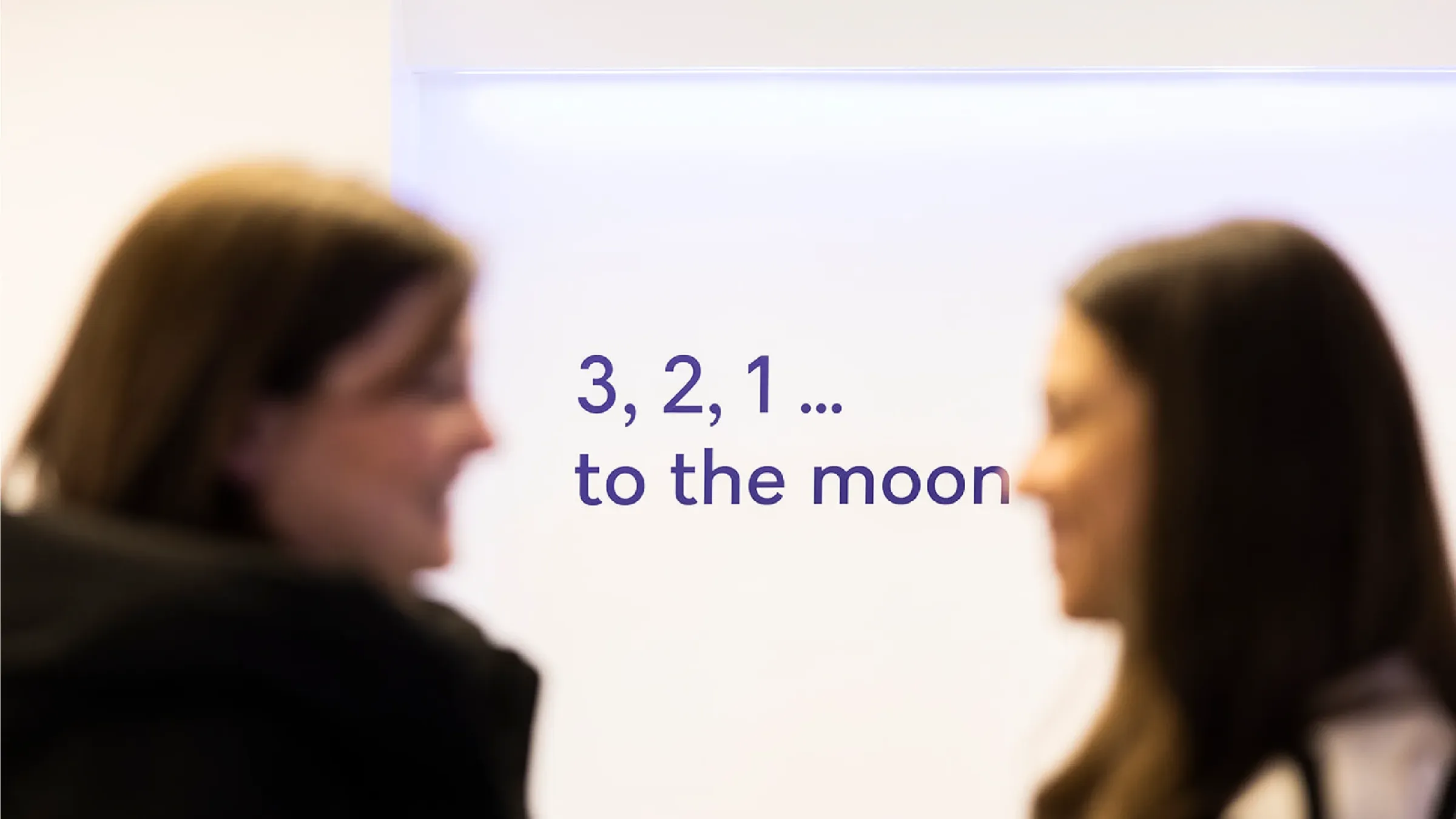 Dos personas conversan frente a una pared con el lema «3, 2, 1… to the moon»