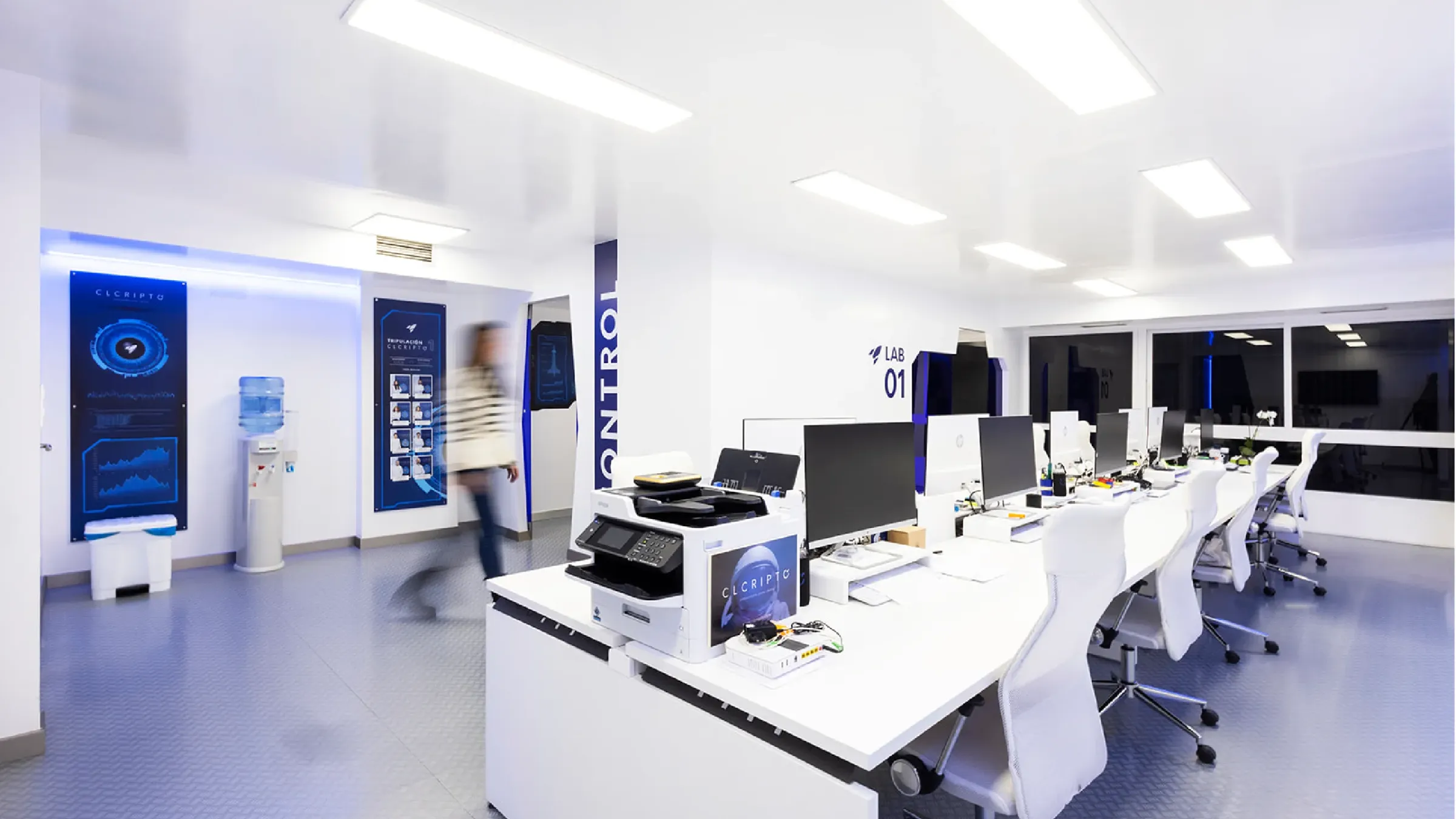 Zona de trabajo de CLCripto, blanca y luminosa, con paneles azules de la marca en la pared y el rótulo «Control»