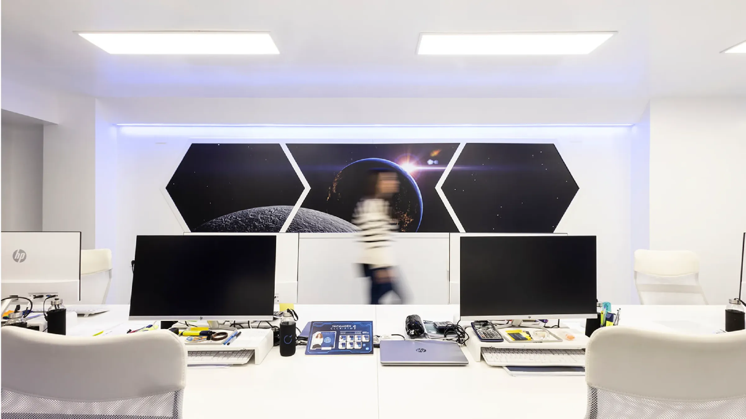 Puesto de trabajo con varias pantallas frente a un mural de hexágonos con la Luna y el espacio
