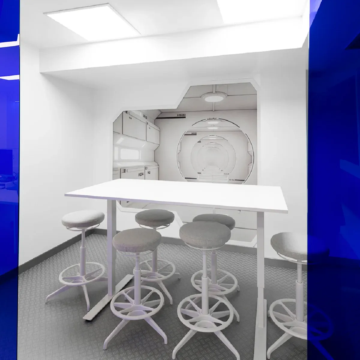 Sala de reuniones blanca con mesa alta y taburetes, inspirada en el interior de una nave espacial