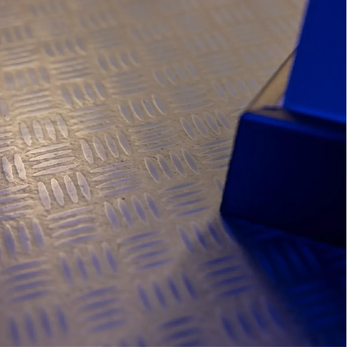 Detalle del suelo de chapa metálica y de un panel de cristal azul
