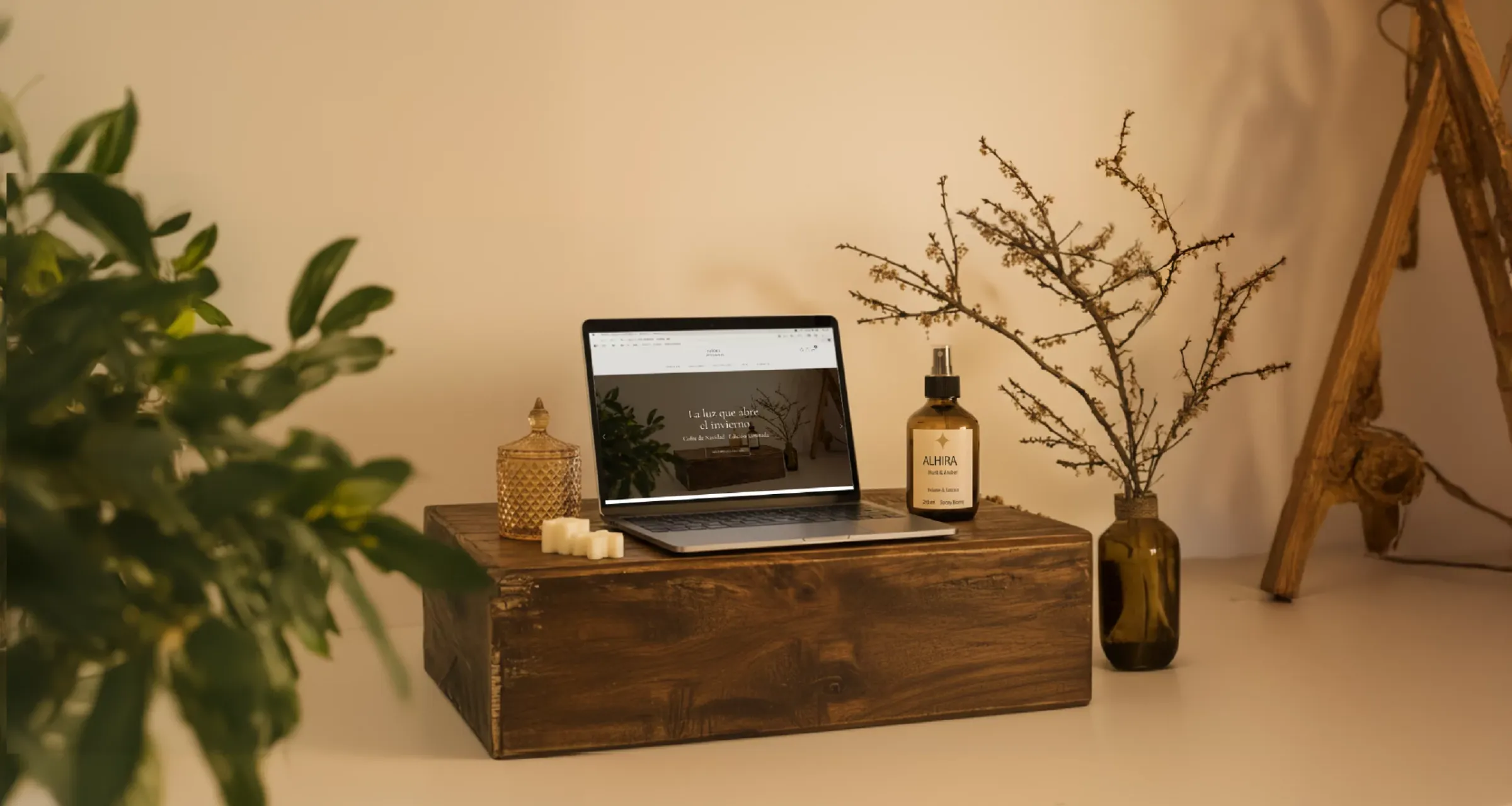 Portátil con la web de Raíces y Trazos sobre una caja de madera, junto a velas, un frasco ámbar y ramas secas
