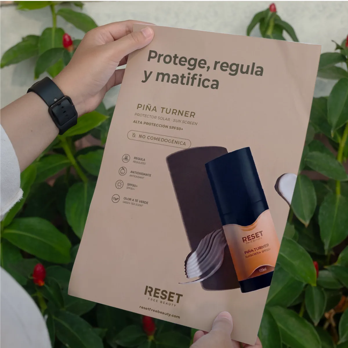 Manos sujetando un cartel de Reset Free Beauty del protector solar Piña Turner entre plantas