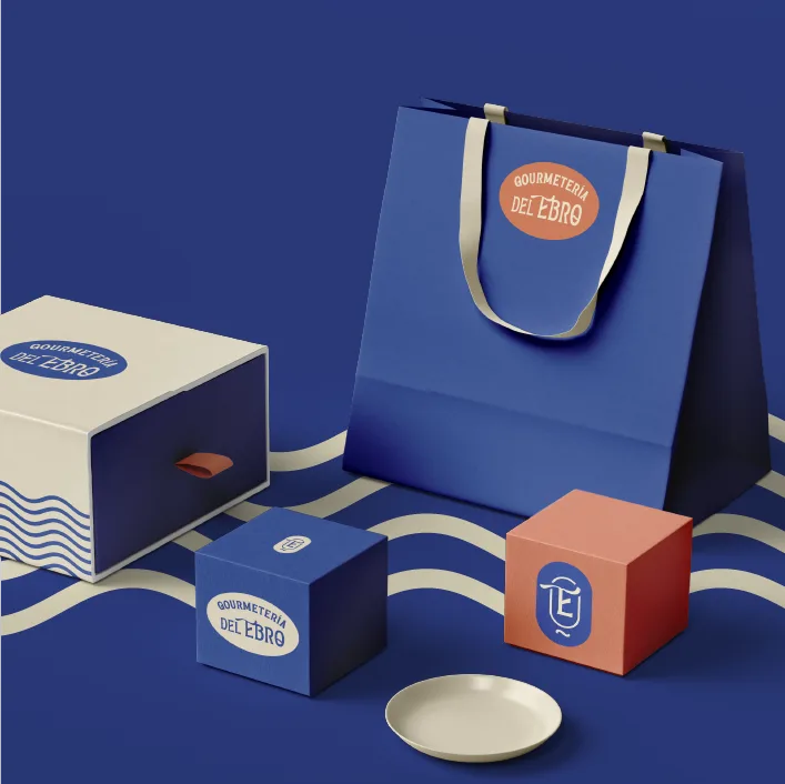 Cajas y bolsa de Gourmetería del Ebro en azul, coral y crema con el sello ovalado de la marca
